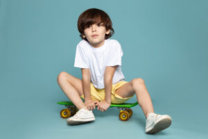 front-view-cute-boy-white-t-shirt-yellow-shorts-riding-green-skateboard-blue-space